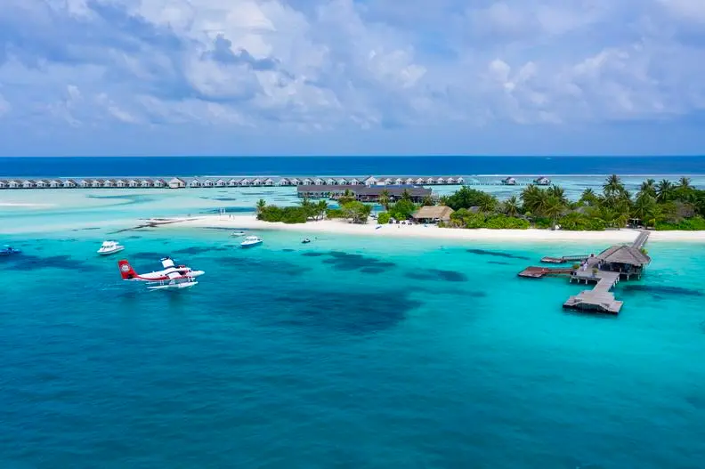Aerial view of LUX South Ari Atoll in the Maldives with overwater villas, white sand beach, turquoise lagoon, and a seaplane docked offshore.