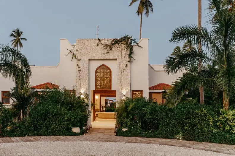 Front view of LUX Marijani in Zanzibar featuring elegant Swahili-inspired architecture, lush greenery, and tropical palm trees at dusk.