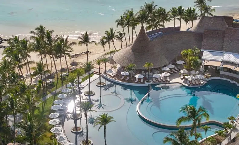 Luxurious beachfront view of LUX Belle Mare Resort & Villas in Mauritius with palm trees, curved pools, and white sand coastline.